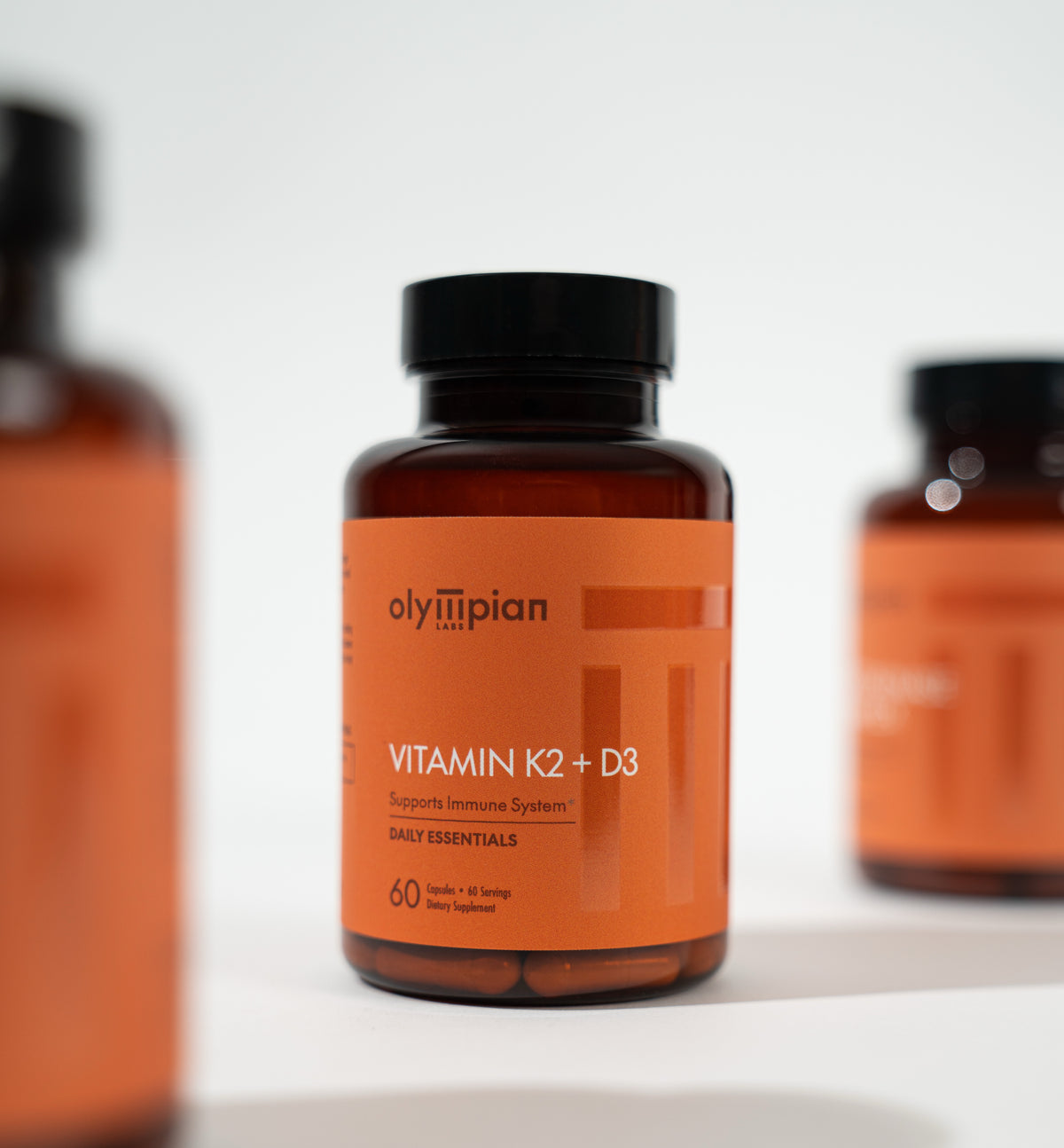 Three bottles of Olympian Vitamin K2 + D3 on a white background