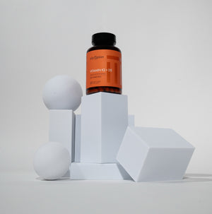 Supplement bottle labeled 'Vitamin K2 + D3' on geometric white blocks with a gray background