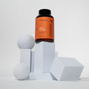 Supplement bottle labeled 'Green Calcium' by Olympian on geometric white blocks with a light gray background