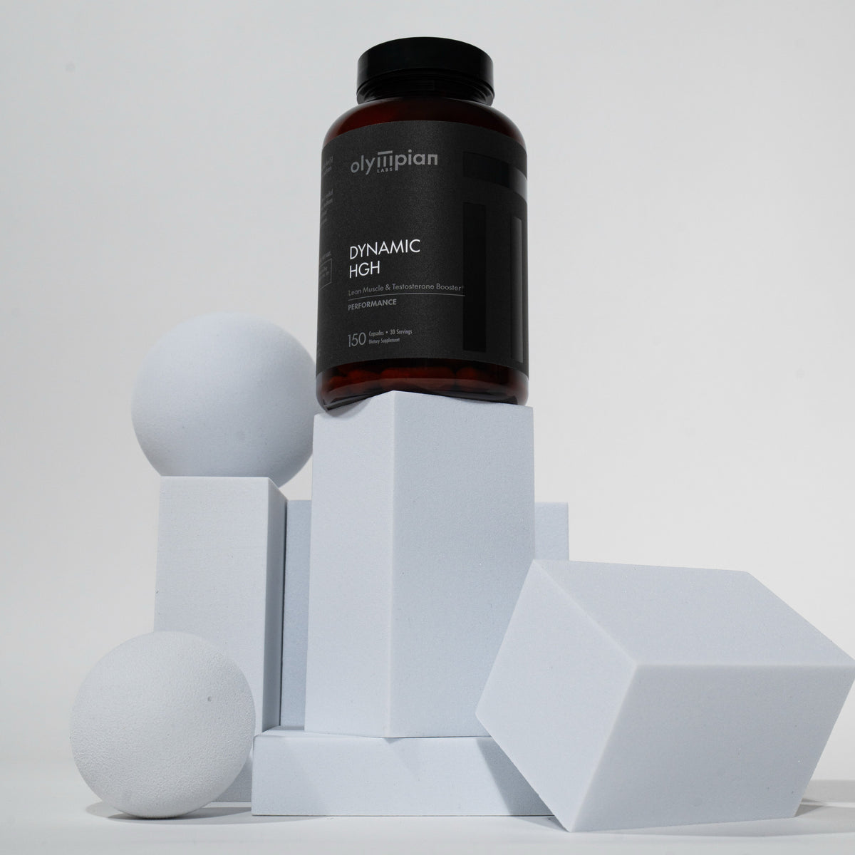 Black supplement bottle labeled 'Olymplan Dynamic High' on geometric white blocks with a plain background