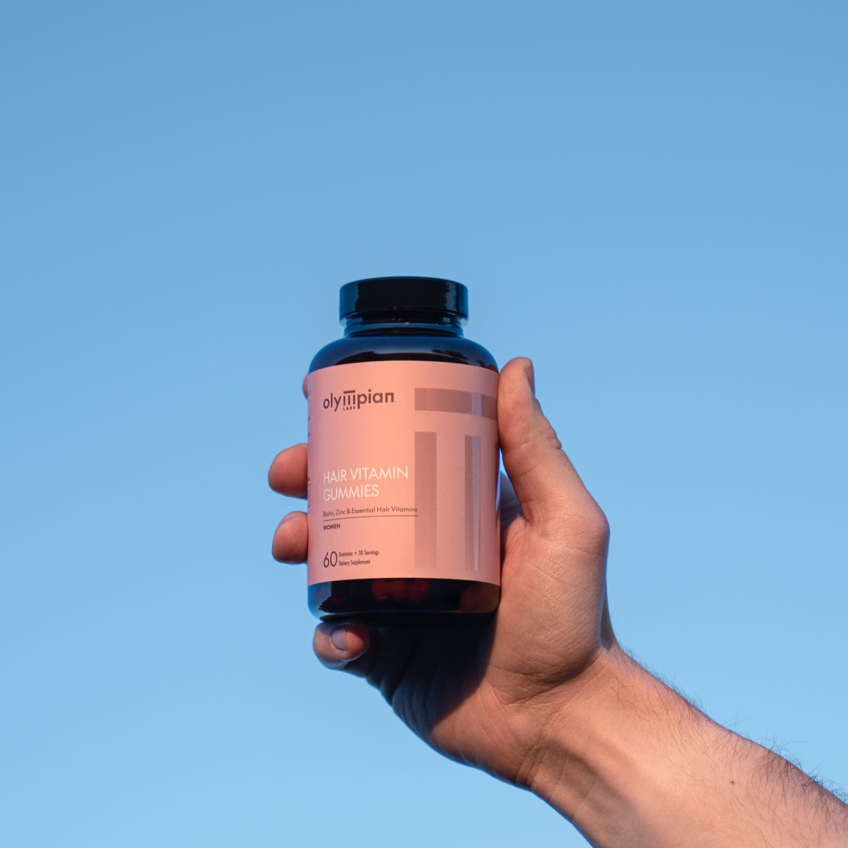 Hand holding a supplement bottle against a clear blue sky