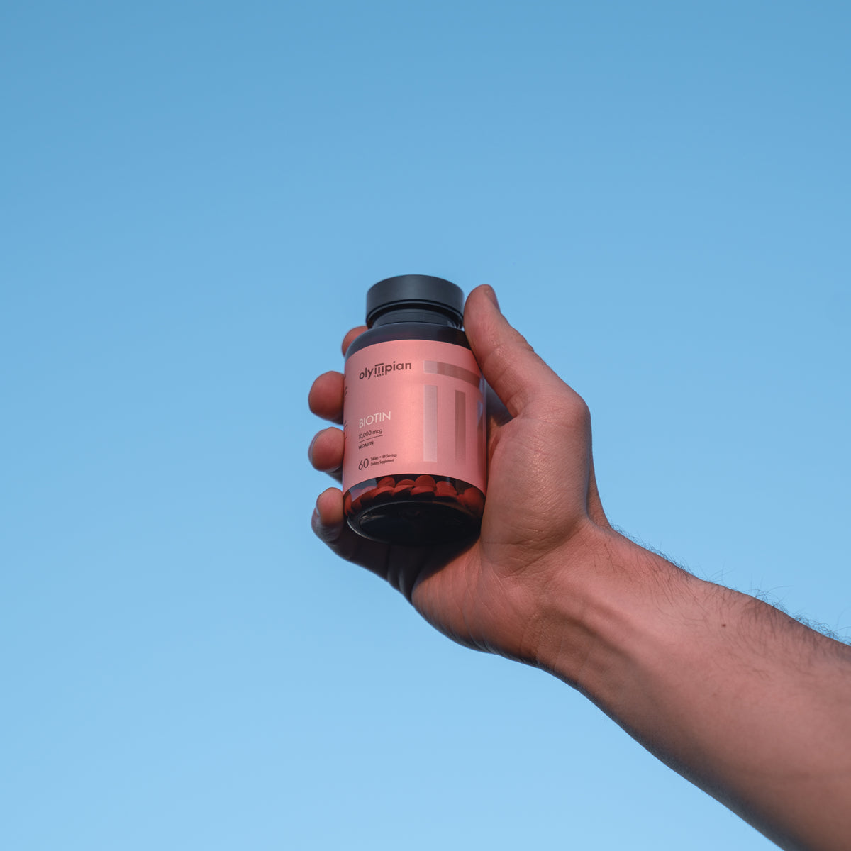 Hand holding a supplement bottle against a clear blue sky