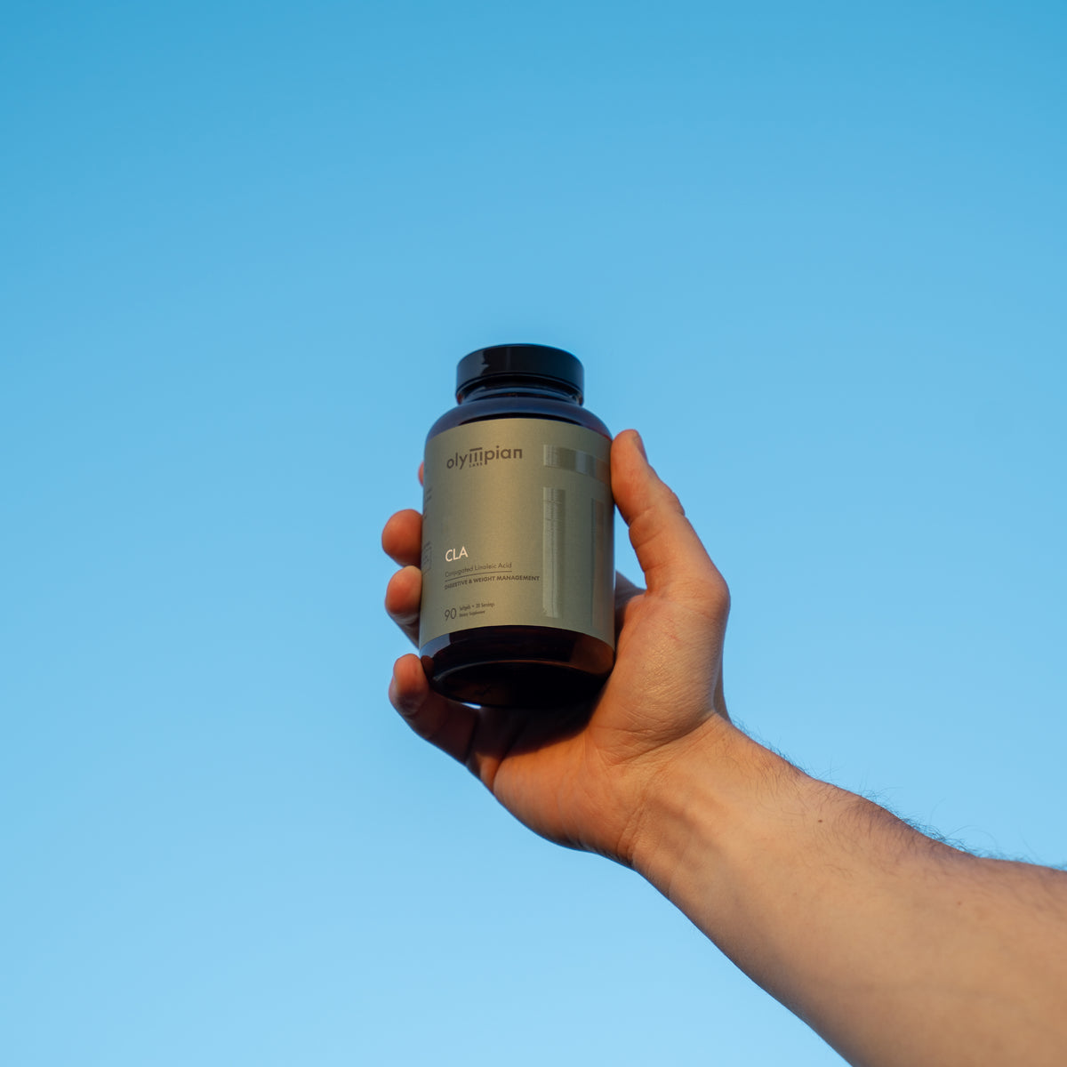 Hand holding a supplement bottle against a clear blue sky