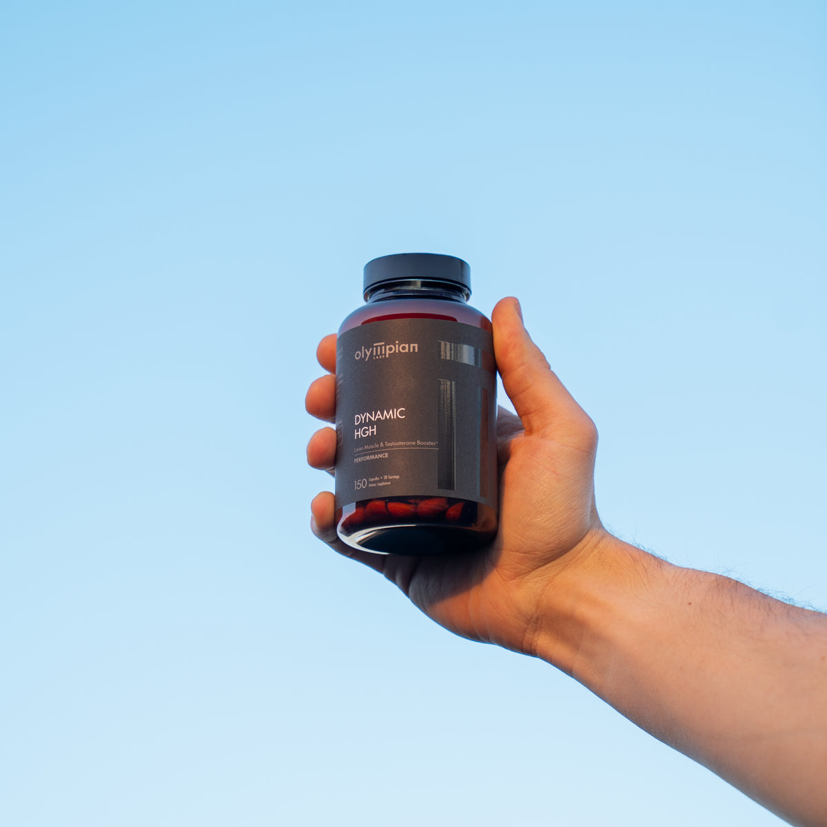 Hand holding a supplement bottle against a clear blue sky