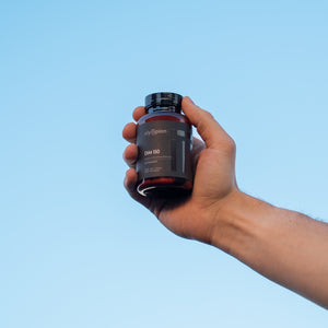 Hand holding a supplement bottle against a clear blue sky