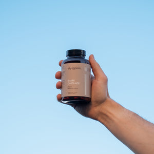Hand holding a supplement bottle against a clear blue sky