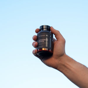 Hand holding a supplement bottle labeled OlympianLabs against a clear blue sky