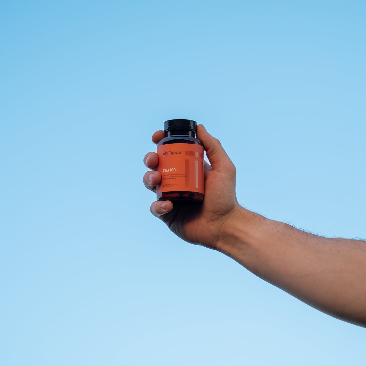 Hand holding a supplement bottle against a clear blue sky