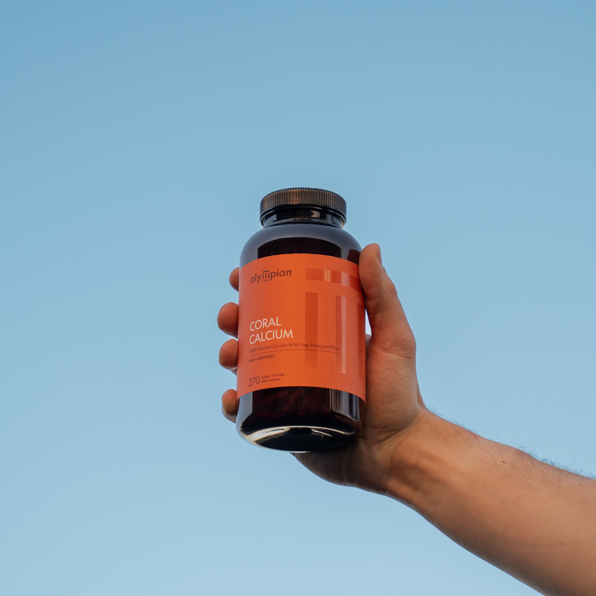 Hand holding a supplement bottle labeled 'Coral Calcium' against a blue background