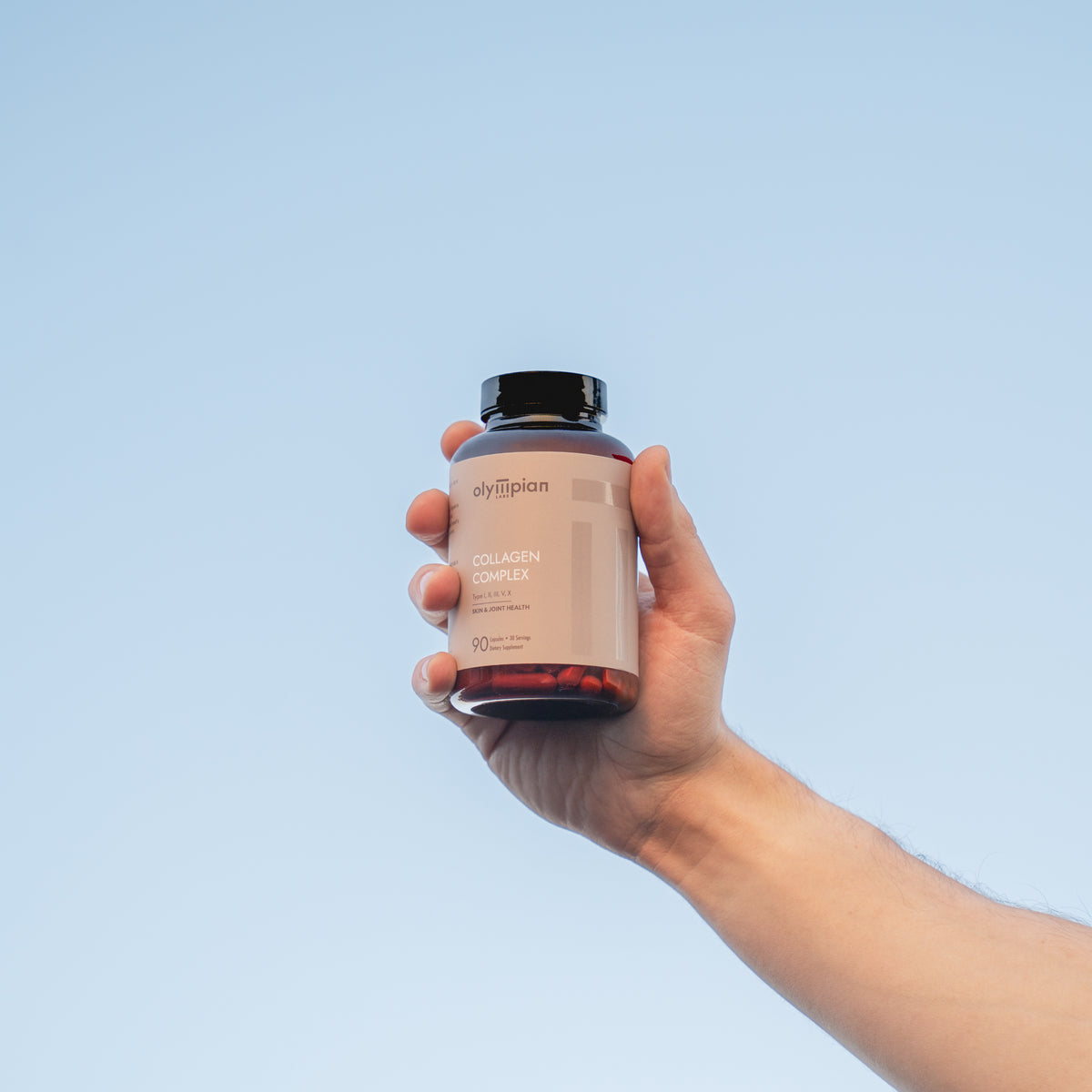 Hand holding a supplement bottle against a clear blue sky