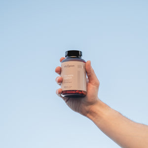Hand holding a supplement bottle against a clear blue sky