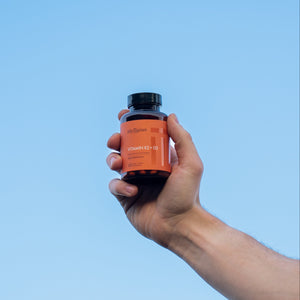 Hand holding a bottle of Vitamin K2+D3 against a clear blue sky