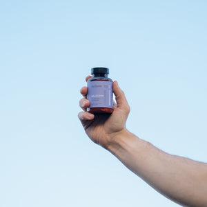 Hand holding a bottle of supplements against a light blue background