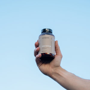 Hand holding a supplement bottle labeled 'Joint Defense' against a clear blue sky