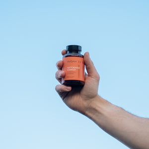 Hand holding a supplement bottle against a clear blue sky