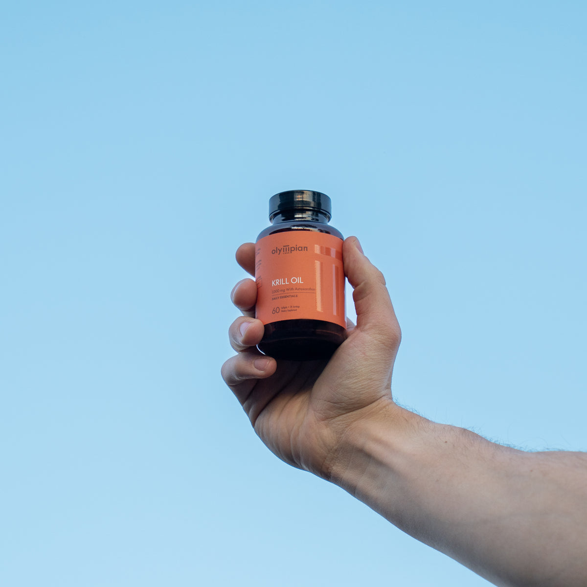 Hand holding a bottle of Krill Oil against a blue background