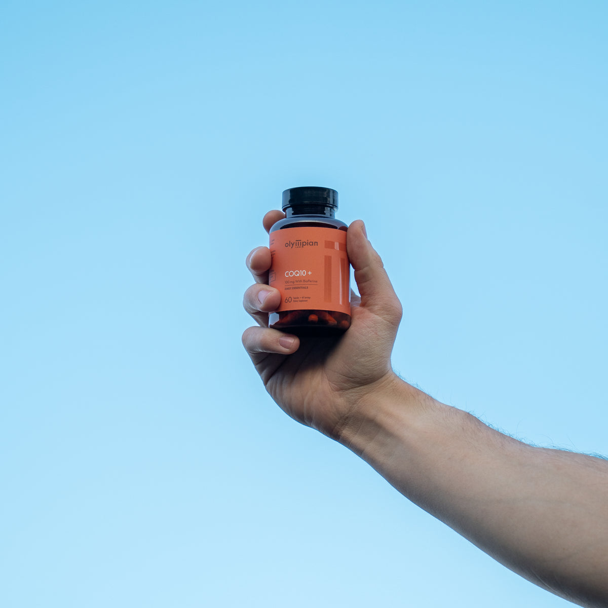 Hand holding a supplement bottle against a clear blue sky