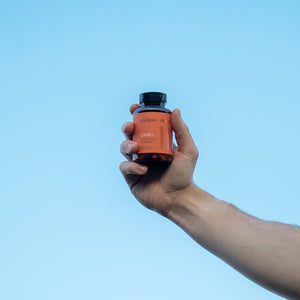 Hand holding a supplement bottle against a clear blue sky