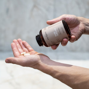 Person pouring supplements from a bottle into their hand against a neutral background