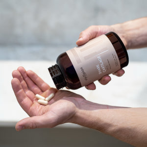 Person holding a bottle of supplements with pills in their hand against a neutral background