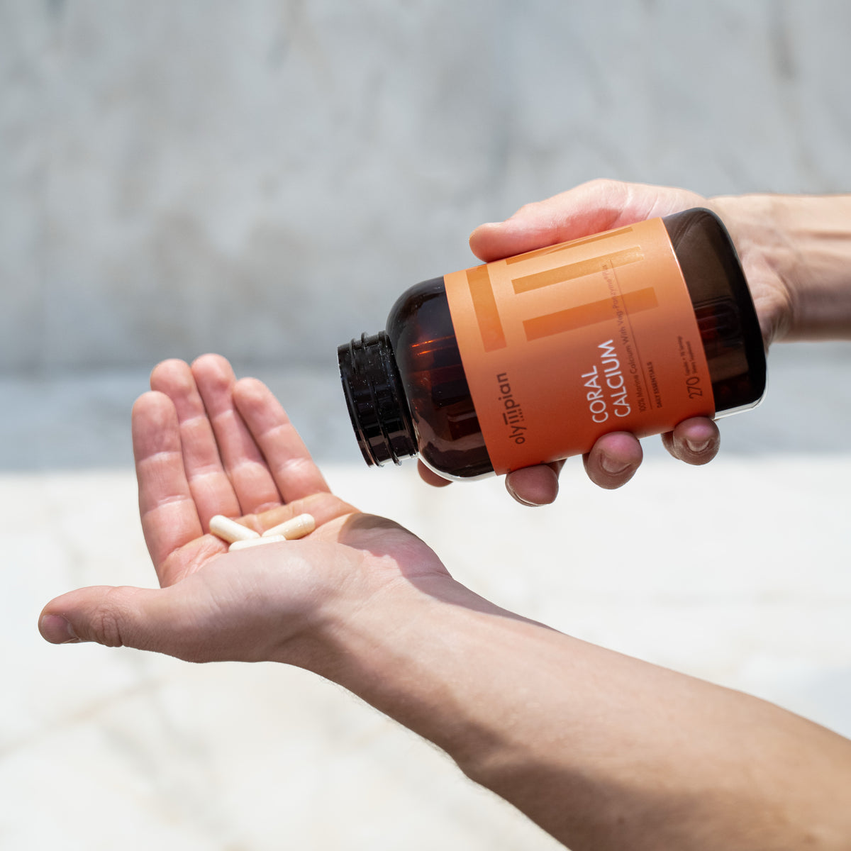 Person holding a bottle of supplements with pills in an open palm against a neutral background