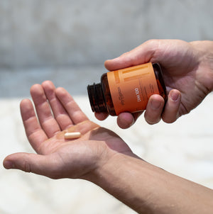 Person holding a bottle of supplements with a pill in their hand