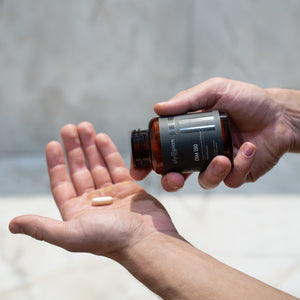 Person holding a bottle of supplements with one pill in their palm against a neutral background