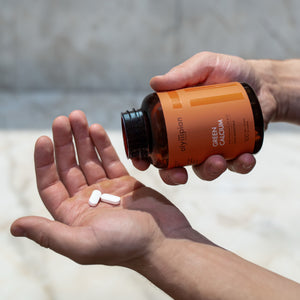 Person holding a bottle of vitamins with two pills in their hand